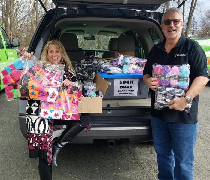Karen and Brian holding socks donations by the back of an SUV.