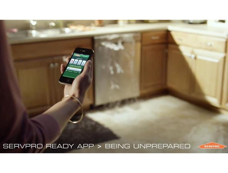 Dishwasher leaking and person holding phone with SERVPRO App on screen,.